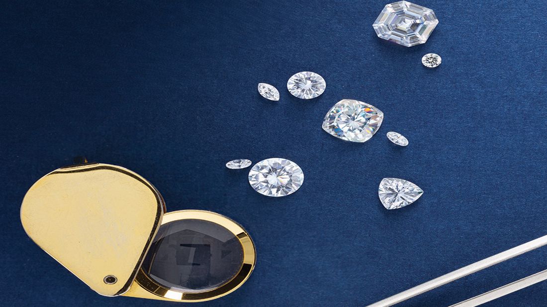 Nine diamonds of various cuts next to a magnifying glass